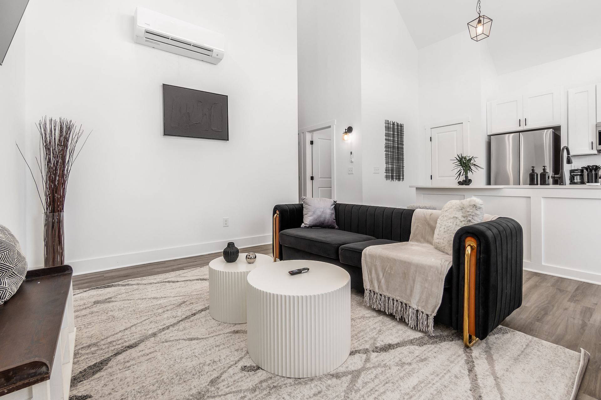 A modern living room with a black sofa, two white round side tables, a grey rug, and a minimalist decor.
