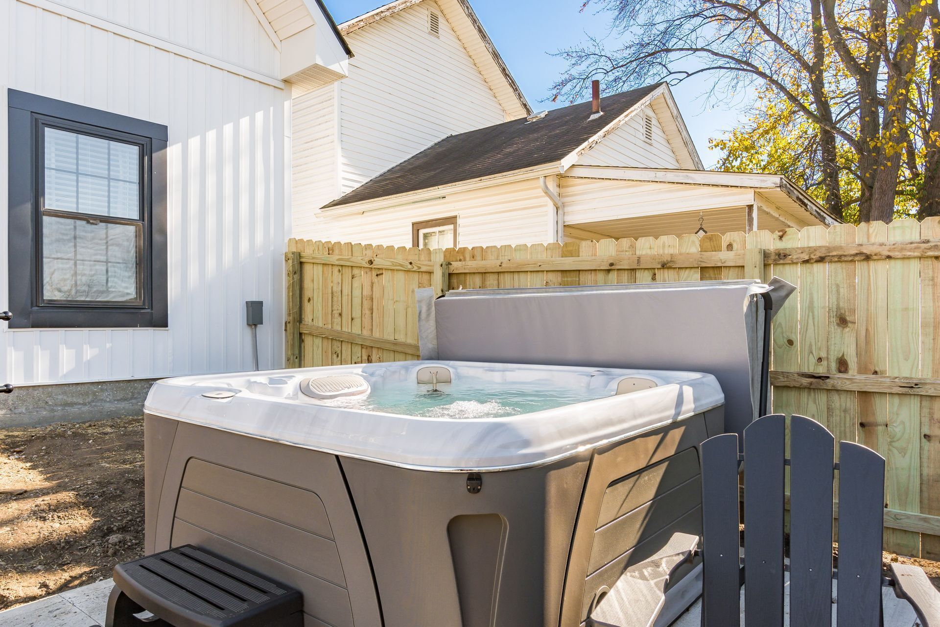 A hot tub in a backyard with a wooden fence and a white house in the background.