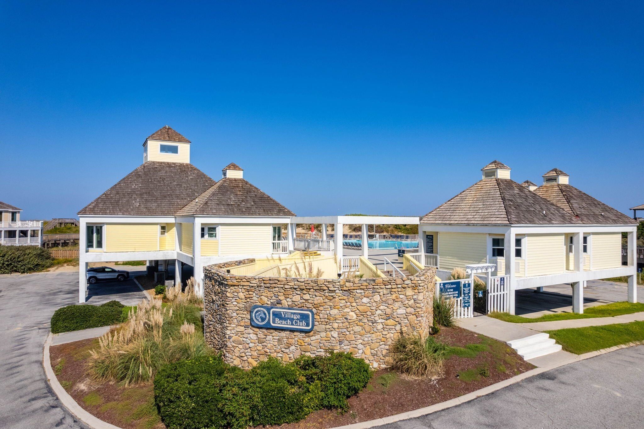A beach club with a stone wall entrance, a sign reading "Village Beach Club", and a covered area with a pool.