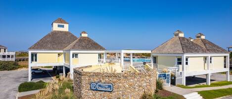 A beach club with a stone wall entrance, a sign reading "Village Beach Club", and a covered area with a pool.