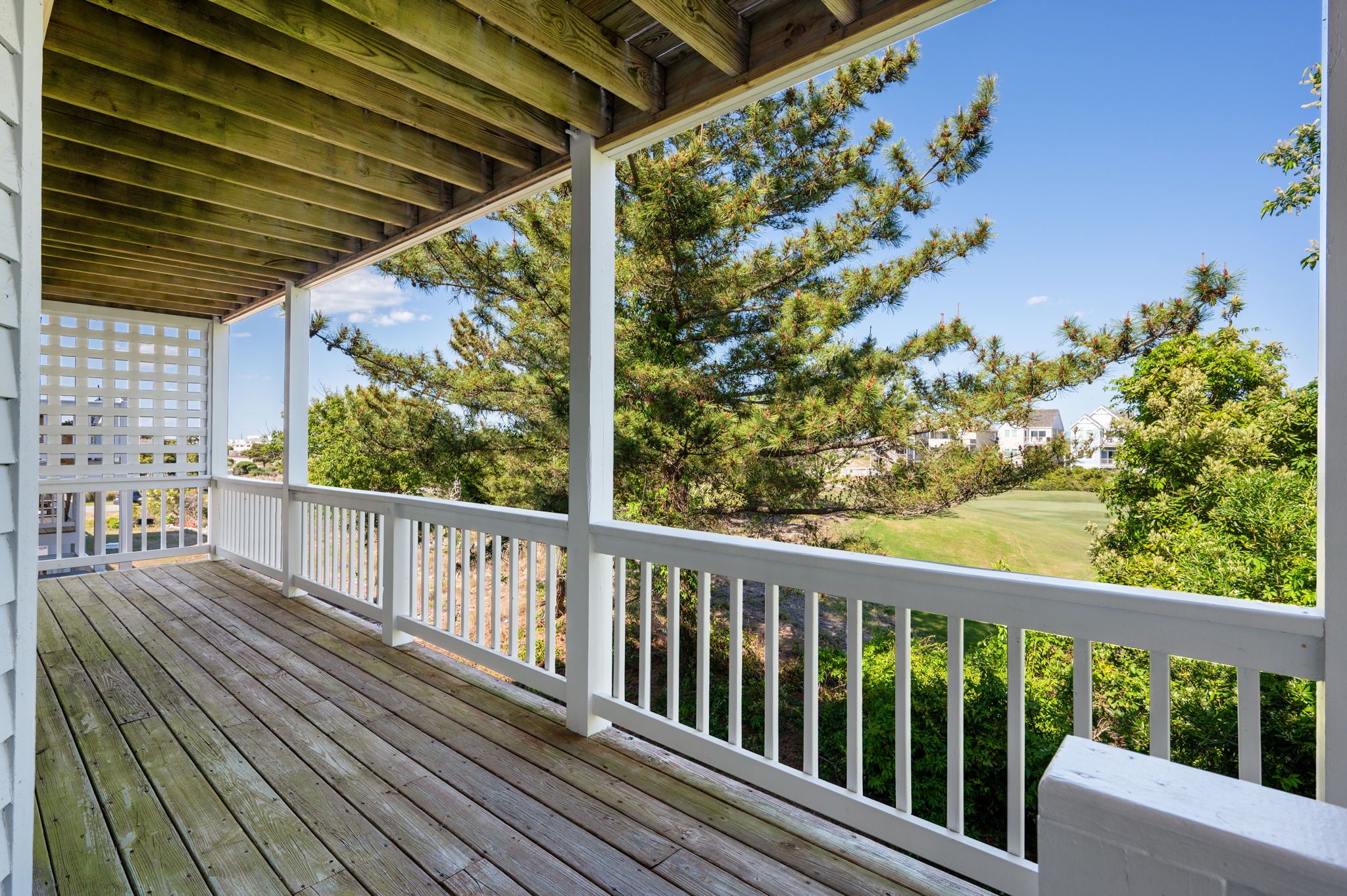 A wooden deck with white railings overlooking a golf course.