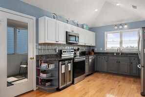 A modern kitchen with white cabinets, a microwave, oven, and refrigerator. There is a window with blinds and a door leading to a balcony.