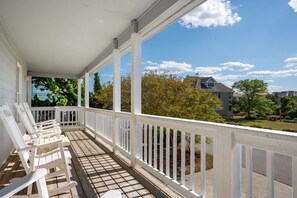 A covered porch with white railings and wooden chairs.