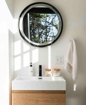 A bathroom with a round mirror, white sink, wooden cabinet, and a towel hanging on the wall. - Dome 3 at Come Spring Farm Glamping - Alpaca Farm (Union)
