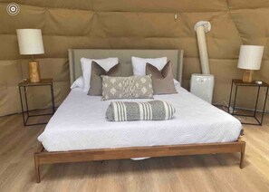 A bed with a wooden frame, white bedding, and multiple pillows. There are two bedside tables with lamps on either side of the bed. - Dome 3 at Come Spring Farm Glamping - Alpaca Farm (Union)