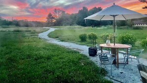Een terras met een tafel en stoelen, een witte parasol en een koffer op een grindpad.