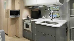 Een kleine keuken met een magnetron, kookplaat, spoelbak en kasten.