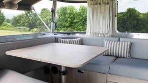 Een compact, modern interieur van een camper met een opklapbare tafel, beklede zitplaatsen en uitzicht op groen buiten.