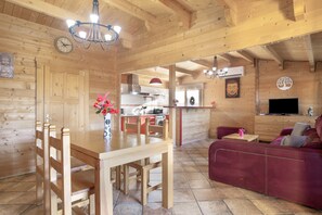 Un interior de madera con una mesa de comedor, sillas, un sofá, un televisor y una zona de cocina.