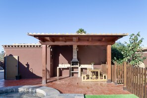 Un patio exterior con una parrilla, asientos y una pérgola.