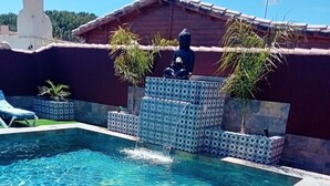 Une piscine agrémentée d’une cascade, entourée de carreaux décoratifs et d’une statue.