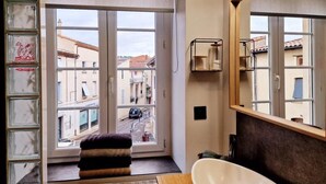 A bathroom with a large window, a white bathtub, and a mirror. - LE DRÔMARDÈCHOIS *** Gîte meublé Ardèche / ECOLODGITE (TOURNON)