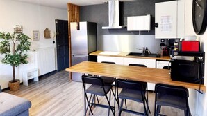 A modern kitchen with a wooden table, black chairs, a refrigerator, a microwave, and a clock on the wall. - LE DRÔMARDÈCHOIS *** Gîte meublé Ardèche / ECOLODGITE (TOURNON)