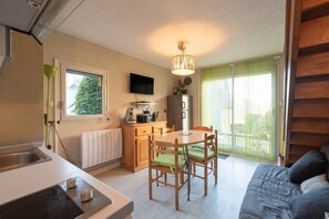 A compact kitchen with a dining area, a TV mounted on the wall, and a sliding glass door leading to a balcony.