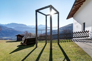 A wooden structure in a yard with a mountain view, a small wooden building, and a white building with a wooden roof.