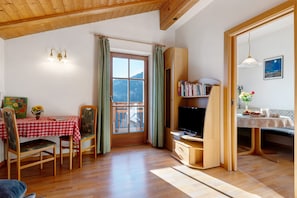 A cozy room with a wooden ceiling, a dining table with chairs, a bookshelf, and a television.