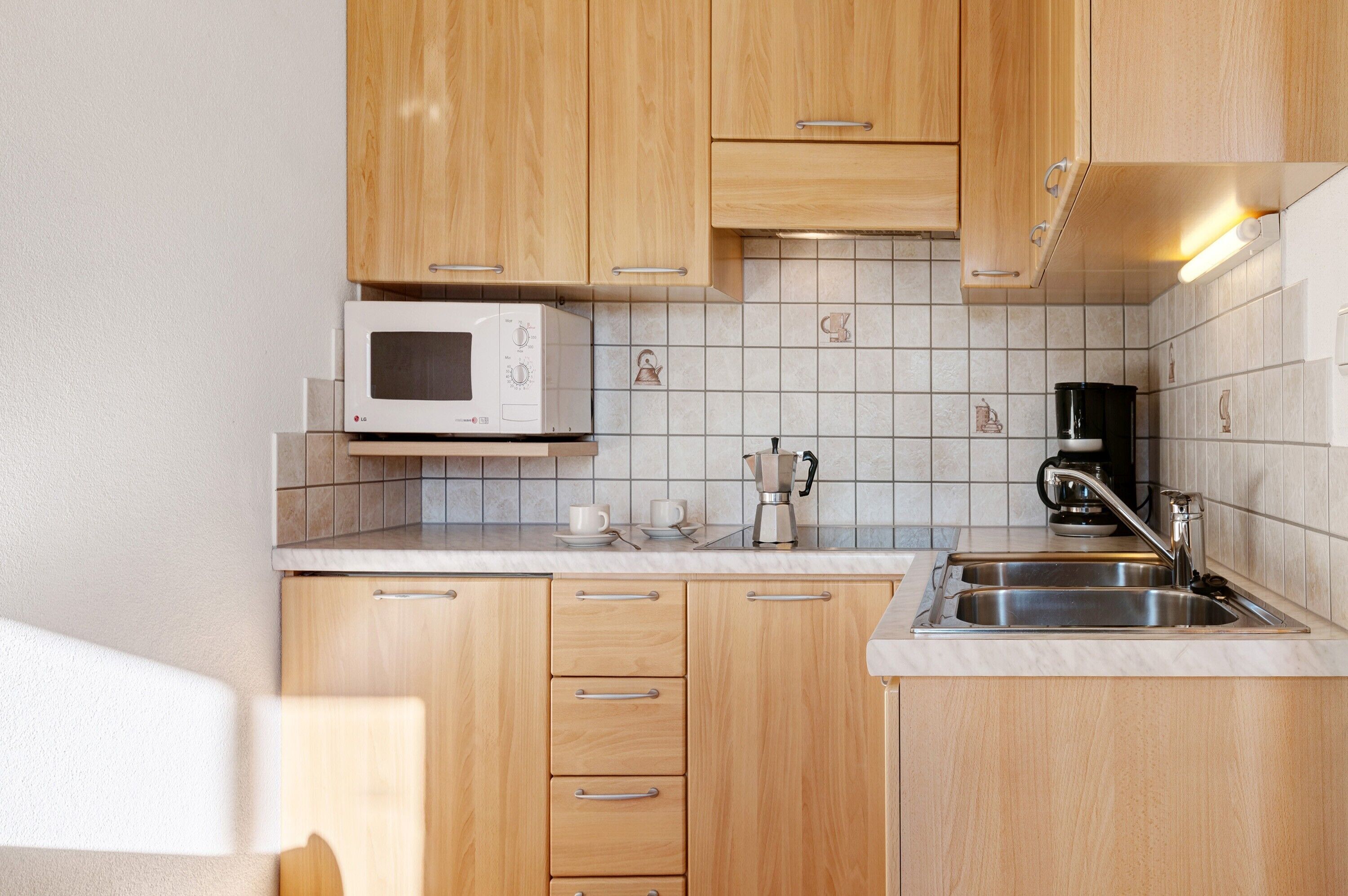A kitchen with wooden cabinets, a microwave, a coffee maker, and a sink.