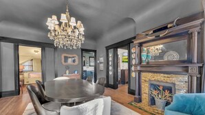 A modern living room with a dark color scheme, a chandelier, a fireplace, and a dining area with a round table and chairs.