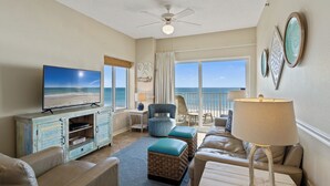 A living room with a TV, wicker ottomans, a ceiling fan, and a view of the ocean. - Tidewater 801 | Pools, Gym, Hot Tub, Wifi | Private Balcony | Ocean Front Views (Orange Beach)