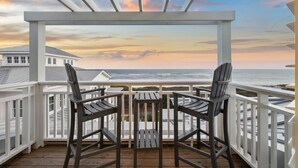 A wooden deck with two Adirondack chairs facing a white railing overlooking a beach. - Beach Front + Pool Front Watercolor Condo | Beach Views of 30A (Watercolor)