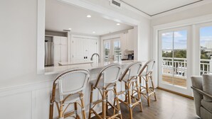 A modern kitchen with white cabinetry, a large island with bar stools, and a view of the balcony. - Beach Front + Pool Front Watercolor Condo | Beach Views of 30A (Watercolor)