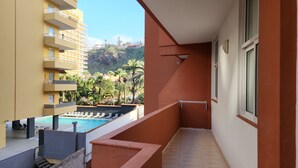 A balcony with a pool, a view of a building, and a mountain in the background.