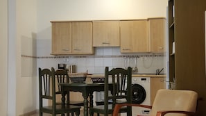 A small kitchen with wooden cabinets, a washing machine, and a dining table with chairs.