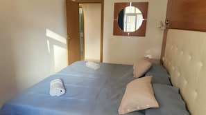 A bedroom with a bed, two pillows, a wall-mounted mirror, and a door leading to another room.