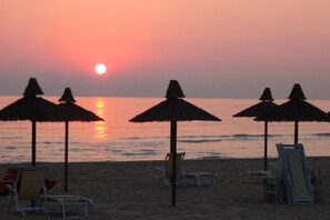 Una playa con sombrillas y sillas, una puesta de sol y agua tranquila.
