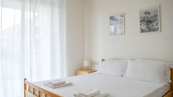 Una camera d'albergo con un letto, un comodino e una finestra con tende leggere.