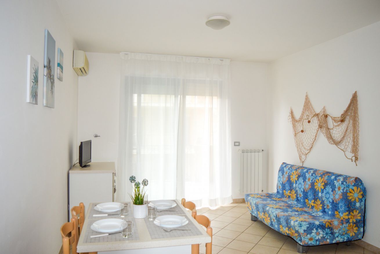Zona pranzo con tavolo apparecchiato per quattro persone, divano e televisione su un mobile.