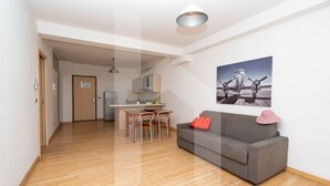 Un grand espace de vie comprenant un canapé gris, une table à manger avec des chaises, et une cuisine en arrière-plan.