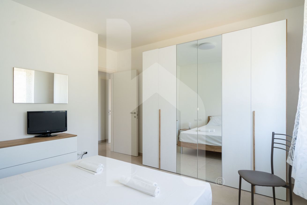 Una camera d'albergo moderna con un letto, una TV, un armadio e una sedia.