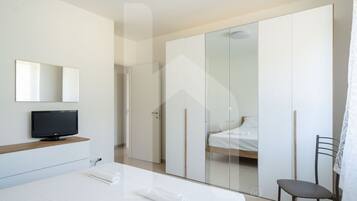 Una camera d'albergo moderna con un letto, una TV, un armadio e una sedia.