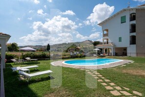 A pool area with lounge chairs, a swimming pool, and a building with balconies. - Homiday - Residence Merope, Ground Floor (Pineto)