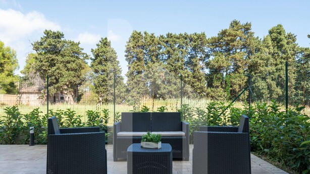 Un espace extérieur aménagé avec des meubles en osier et une petite table, entouré de verdure et d’arbres.