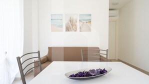 Un coin repas comprenant une table blanche, deux chaises, un canapé beige et un mur orné de trois tableaux encadrés.
