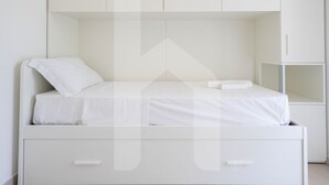 Une chambre à coucher minimaliste, aux murs blancs, comprenant un lit, une table de chevet et une armoire intégrée.
