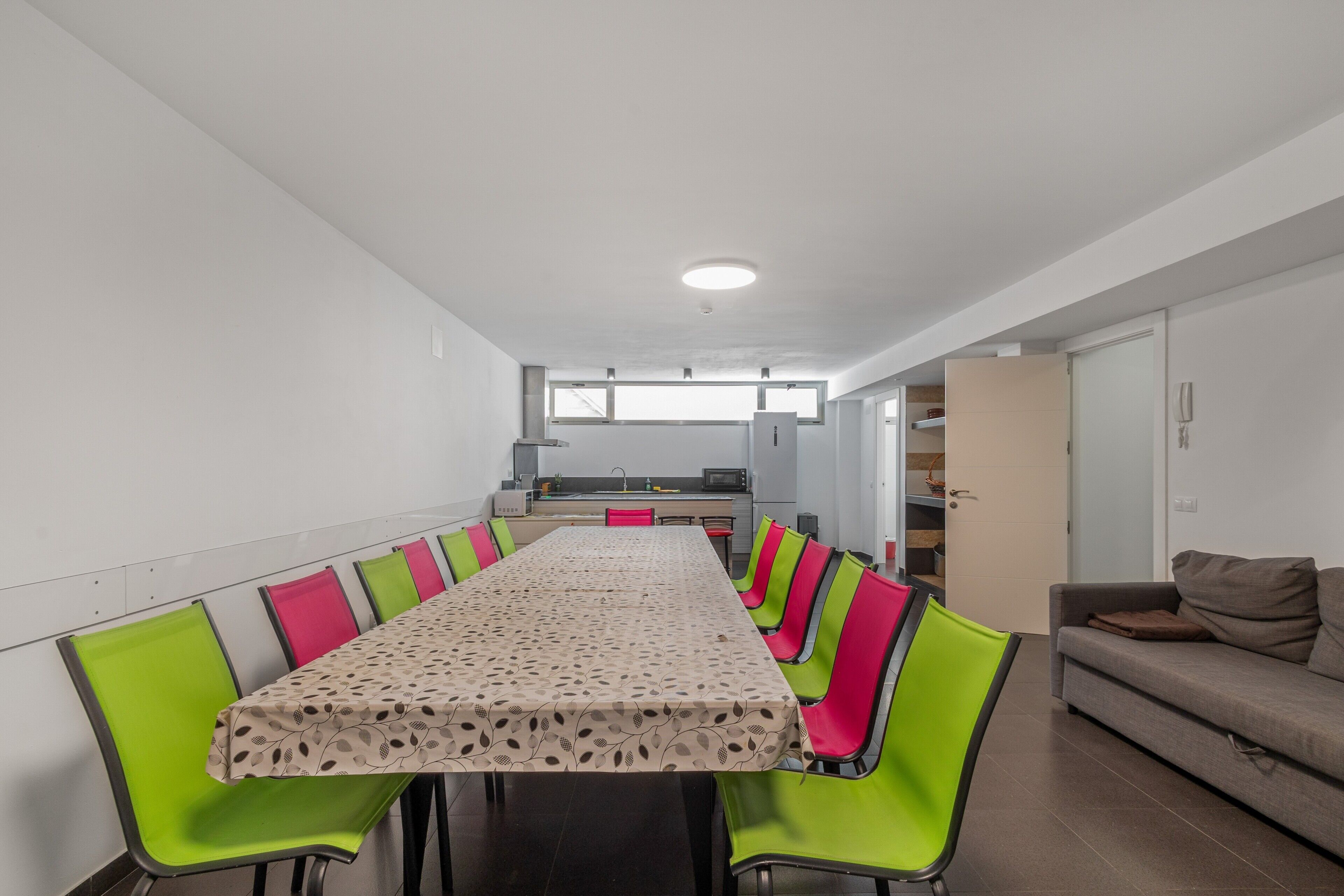 A dining area with a long table, green chairs, and a kitchen in the background.