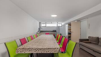 A dining area with a long table, green chairs, and a kitchen in the background.