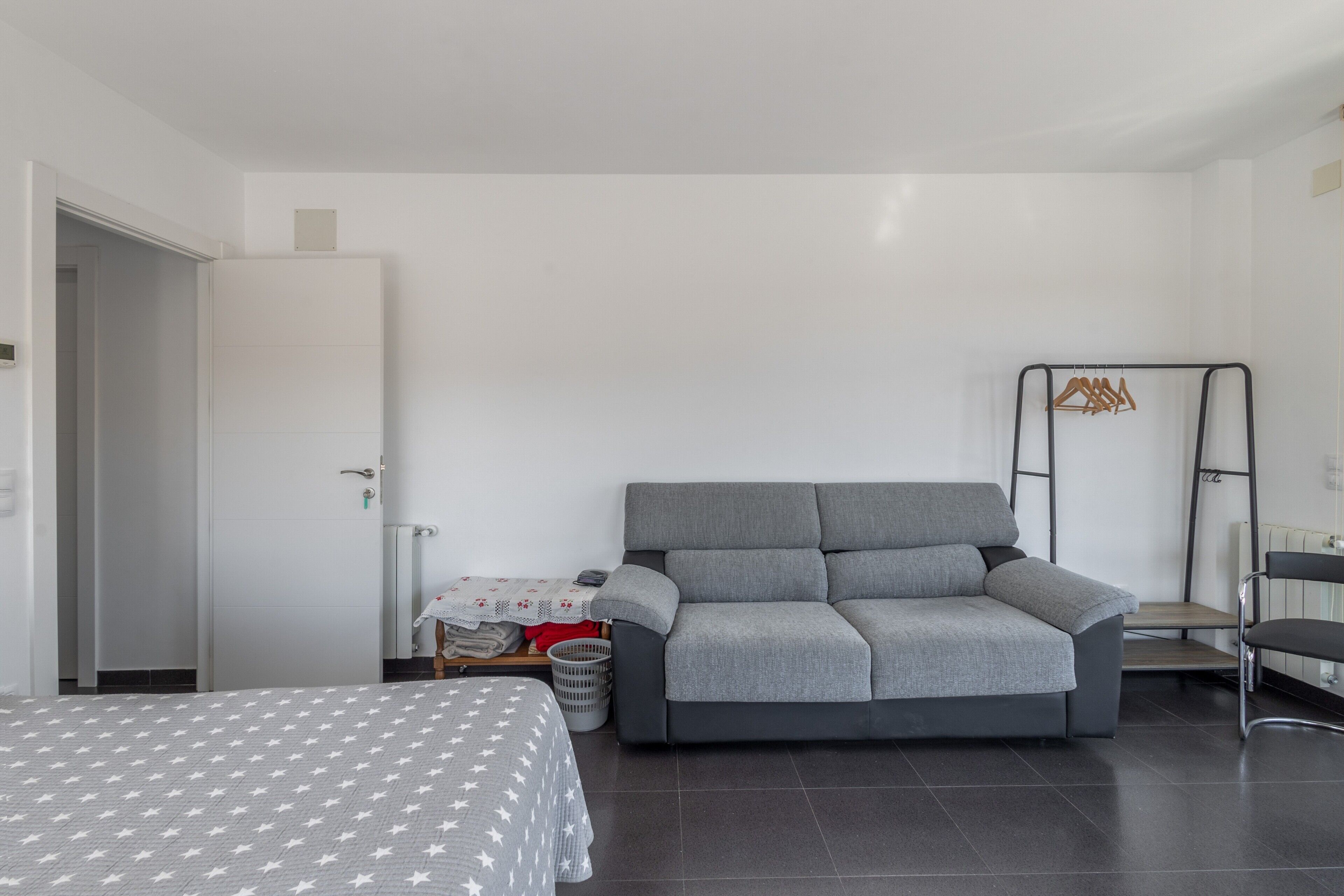 Una stanza moderna con un divano grigio, un letto con copriletto a motivi stellati, un termosifone e un attaccapanni a parete.