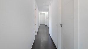 A long, narrow hallway with white walls and a dark floor, leading to a door at the end.