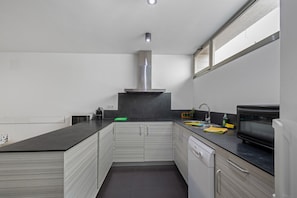 Cozinha moderna com bancada preta, coifa de aço inoxidável e lava-louças.