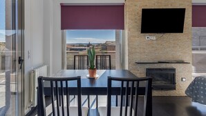 A dining area with a table and chairs, a potted plant, a fireplace, and a TV mounted on a brick wall.