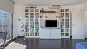 A modern living room with a large bookshelf, a flat-screen TV, and a tripod.