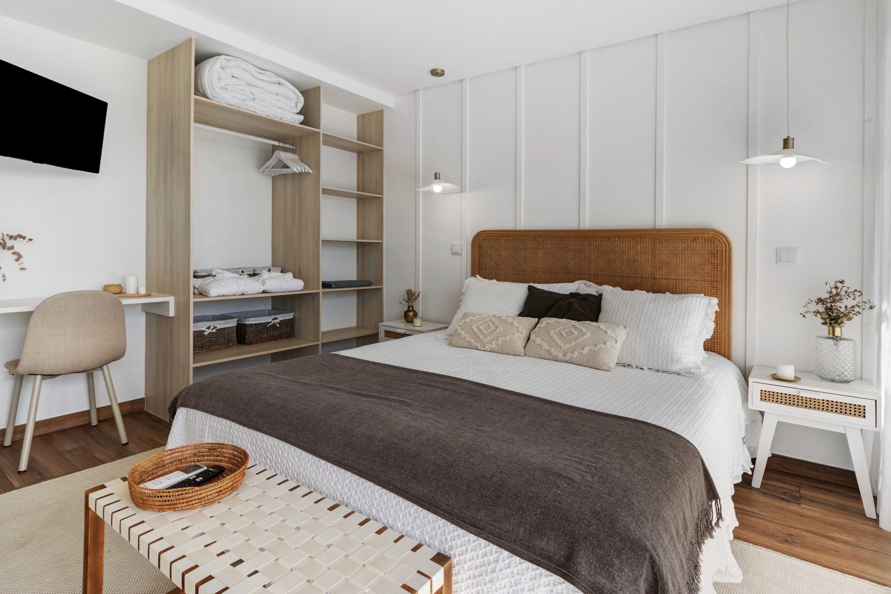 Ein Schlafzimmer mit einem großen Bett, einem Nachttisch, einem Sessel, einem Kleiderschrank und einem an der Wand befestigten Fernseher.