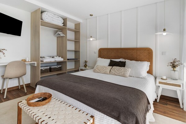 Un dormitorio con una cama grande, una mesita de noche, una silla, un armario y un televisor fijado a la pared.