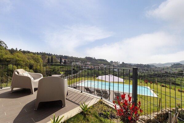 Zona junto a la piscina con mobiliario exterior, vista al paisaje y piscina cercada.