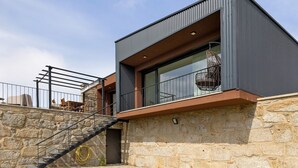 Un edificio moderno con un muro de piedra, una escalera de metal y un balcón con mobiliario exterior.