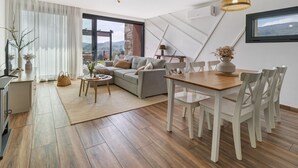 Una sala de estar moderna con sofá, mesa de comedor, sillas y vistas amplias a través de grandes ventanales.